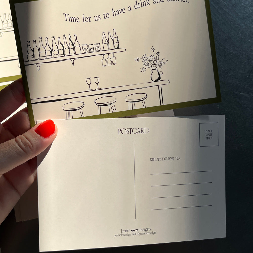 
                  
                    Hand holding a decorative postcard with text and illustrations on a dark surface
                  
                