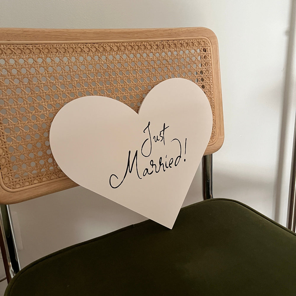 
                  
                    Heart-shaped card with 'Just Married!' text on a textured surface
                  
                